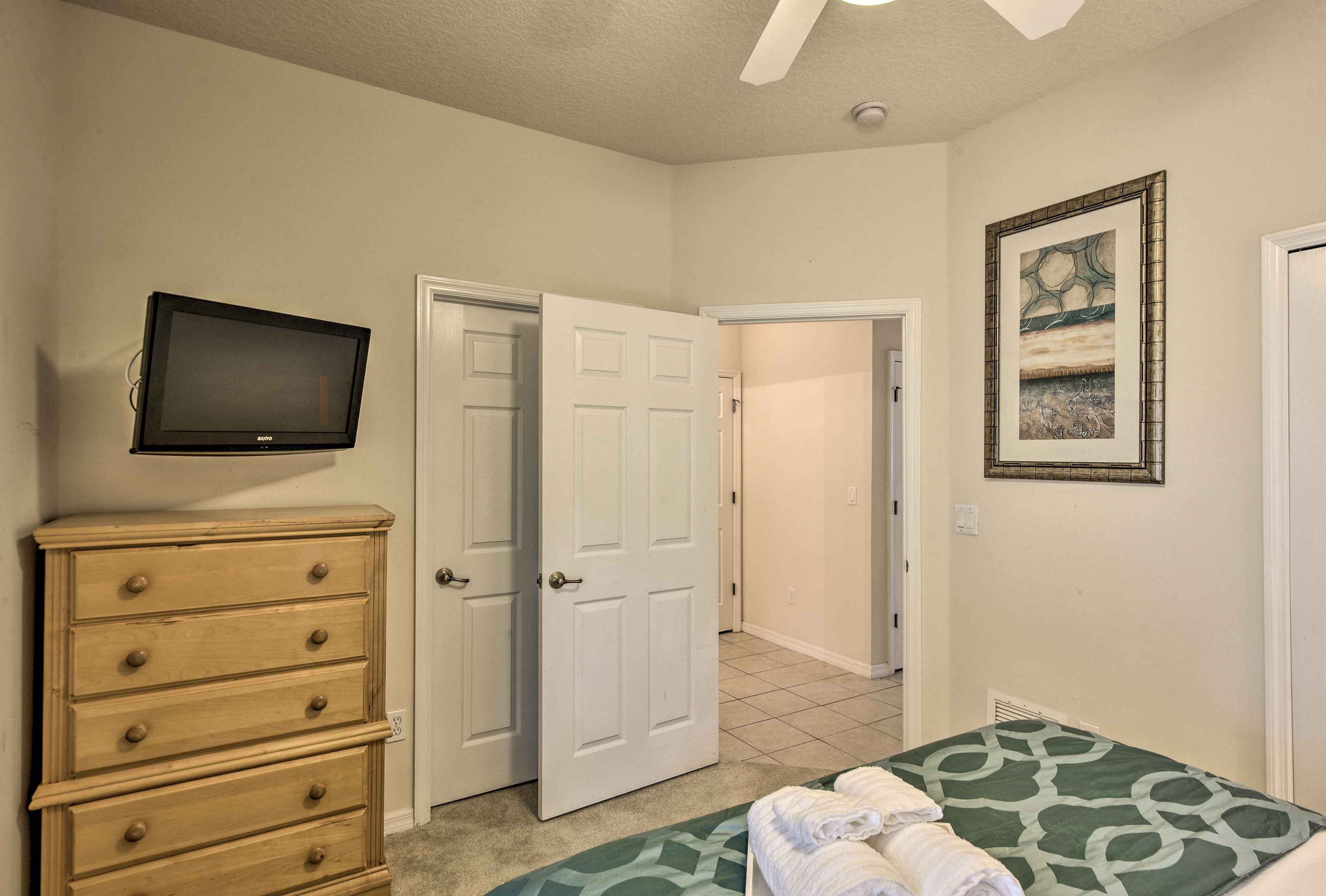 A bedroom with a bed, a dresser, a television, and a door leading to another room.