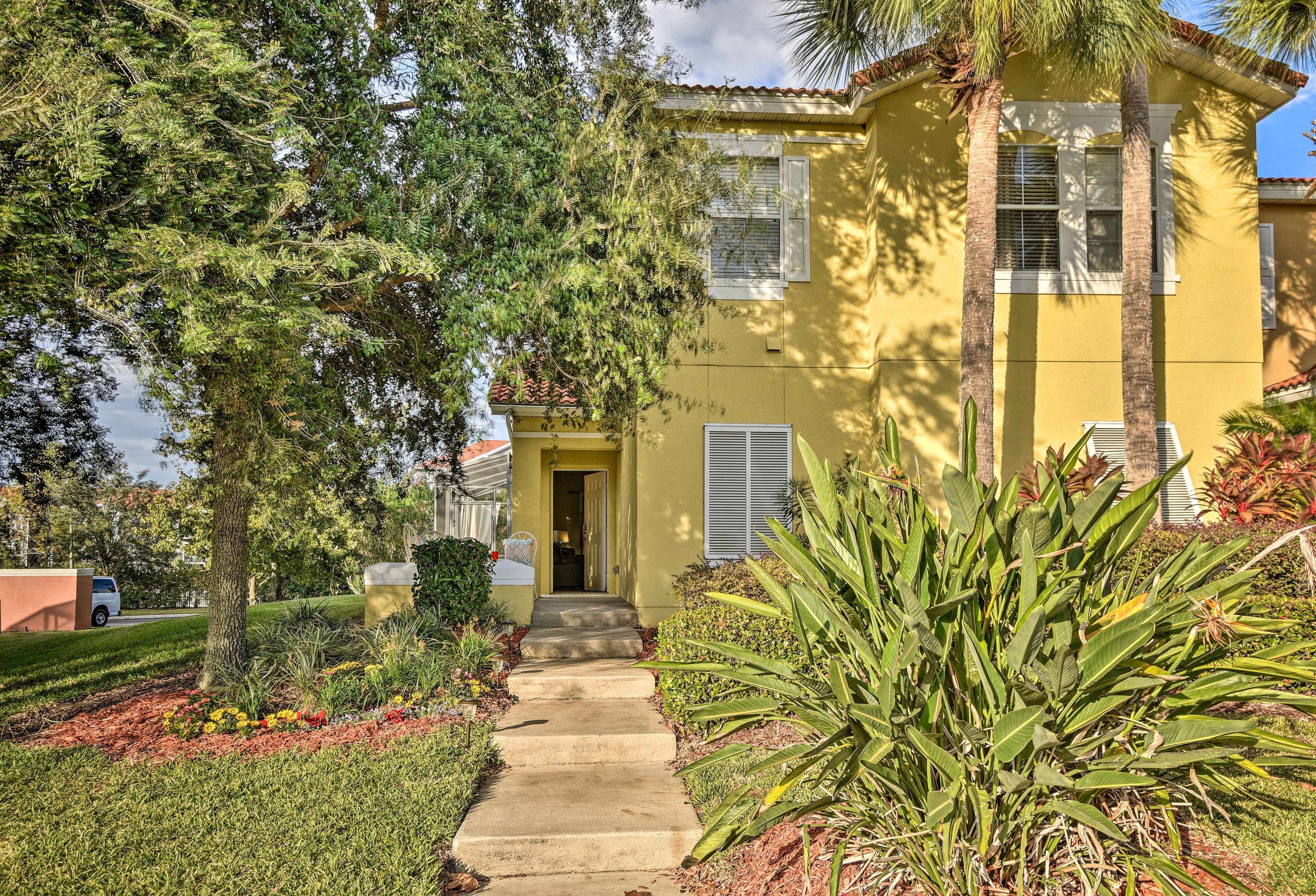 A yellow house with a front door, a concrete pathway, and a garden with various plants.
