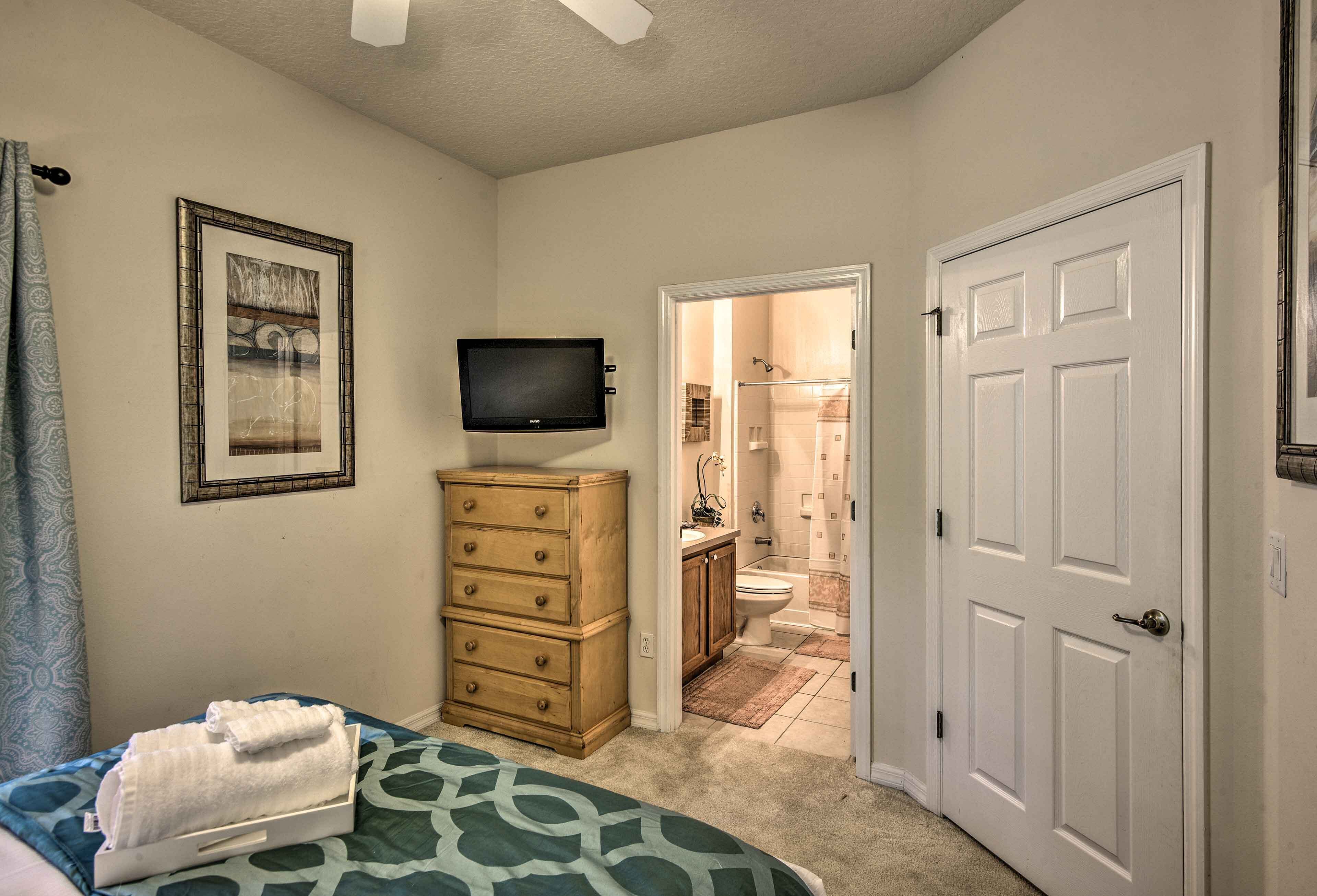 A bedroom with a bed, a dresser, a television, and a bathroom visible through an open door.