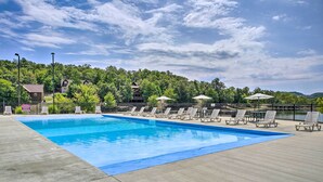 A swimming pool with lounge chairs and umbrellas, surrounded by a fence, with buildings and trees in the background. - Expansive Townhome w/ Game Room & Community Pool (Branson West)