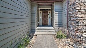 A house with a front porch, a stone wall on one side, and a wooden door with glass panels. - Expansive Townhome w/ Game Room & Community Pool (Branson West)