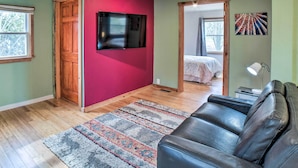 A room with a wooden door, a flat-screen TV mounted on a red wall, a black leather couch, and a patterned rug on the wooden floor. - Indiana Vacation Rental Near Lake Michigan (Valparaiso)