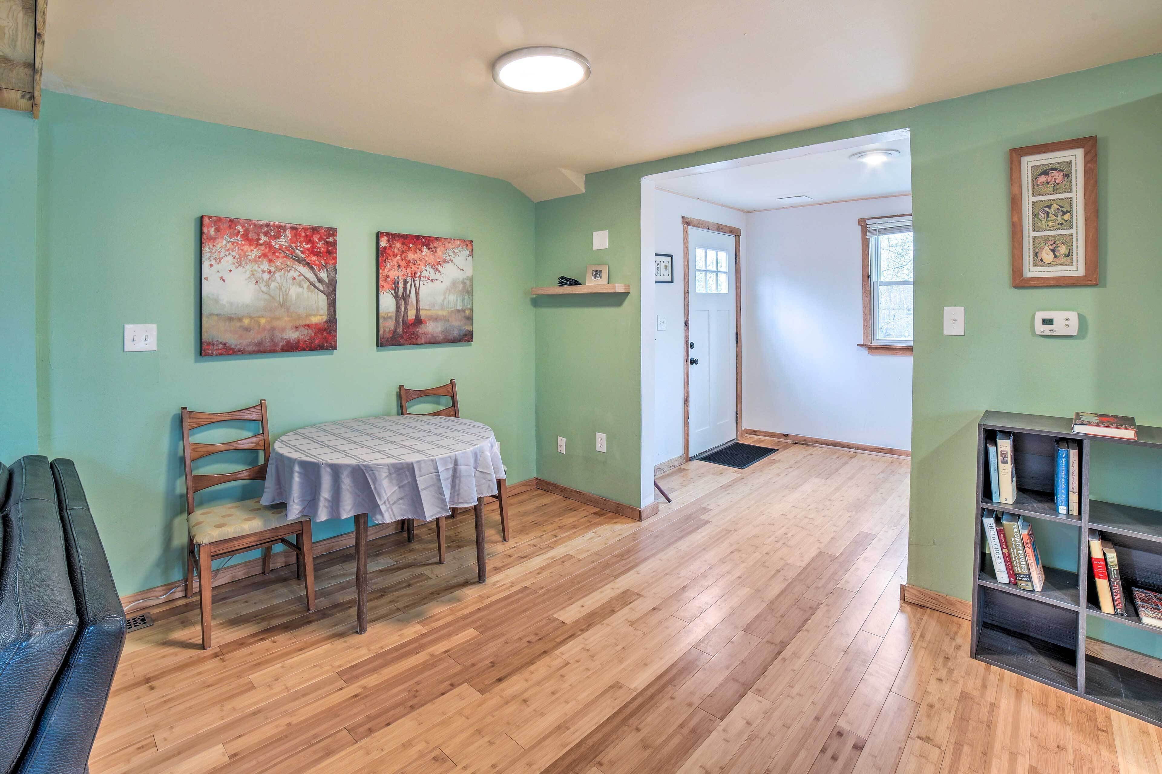 A dining area with a table and chairs, a bookshelf, and two paintings on the wall.