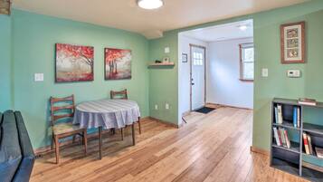 A dining area with a table and chairs, a bookshelf, and two paintings on the wall.