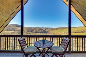 Una terraza de madera con una mesa y dos sillas, con vistas a un paisaje pintoresco.