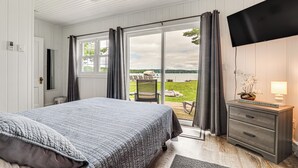 Ein Schlafzimmer mit einem großen Bett, einem an der Wand montierten Fernseher, einem Schreibtisch mit Lampe und einer Glastür zum Patio.
