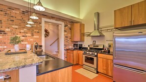 A modern kitchen with a brick wall, wooden cabinets, stainless steel appliances, and pendant lighting. - Pet-friendly Cottage With Game Room & Fire Pit! (Reva)
