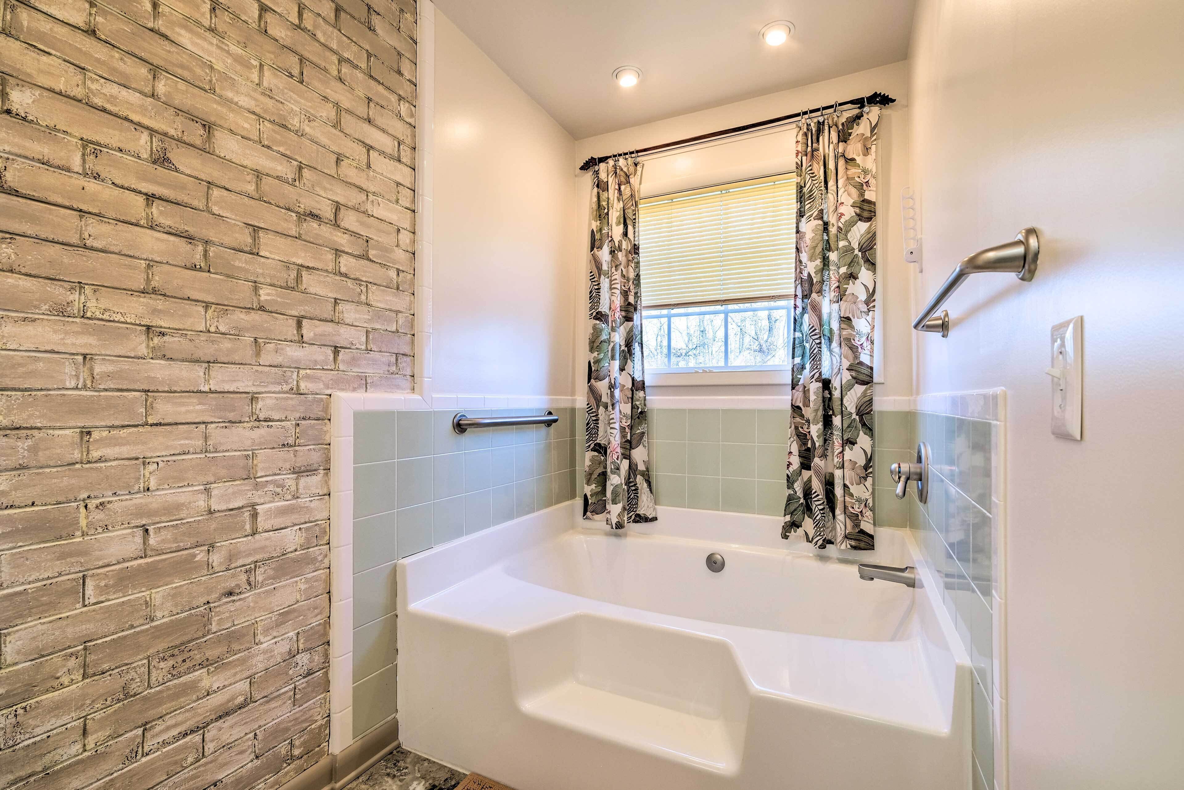 A bathroom with a brick wall, a white bathtub, and a window with a curtain.