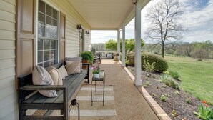 A covered porch with a wooden bench, a small table with a potted plant, and a view of a grassy landscape. - Pet-friendly Cottage With Game Room & Fire Pit! (Reva)