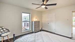 A bedroom with a bed, a ceiling fan, a window, a dresser, and a door.