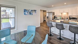 A modern kitchen with white cabinets, a stainless steel refrigerator, and a bar area with stools.