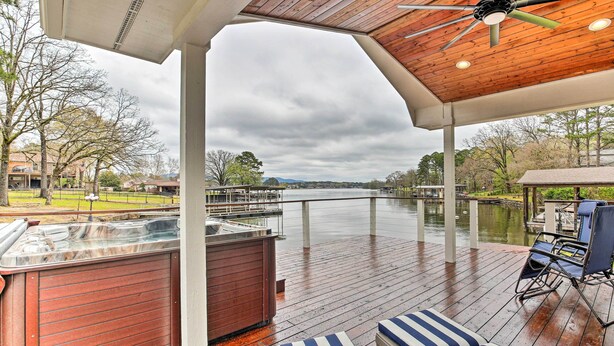 A covered outdoor deck with a hot tub, lounge chairs, and a view of a river.