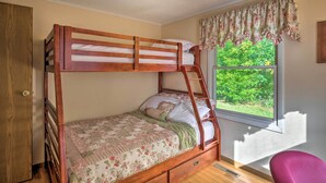 Una cama litera con una colcha estampada de flores, un armario de madera, una ventana con vistas a la vegetación y una silla rosa.