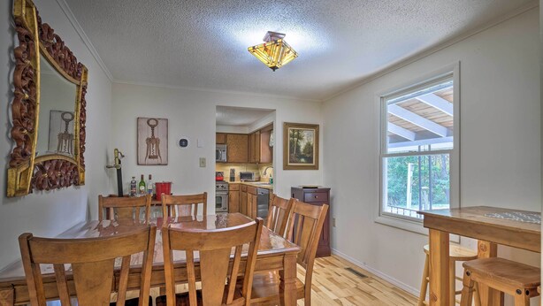 Un comedor con sillas de madera y una mesa, una cocina al fondo y una ventana con vistas a árboles.