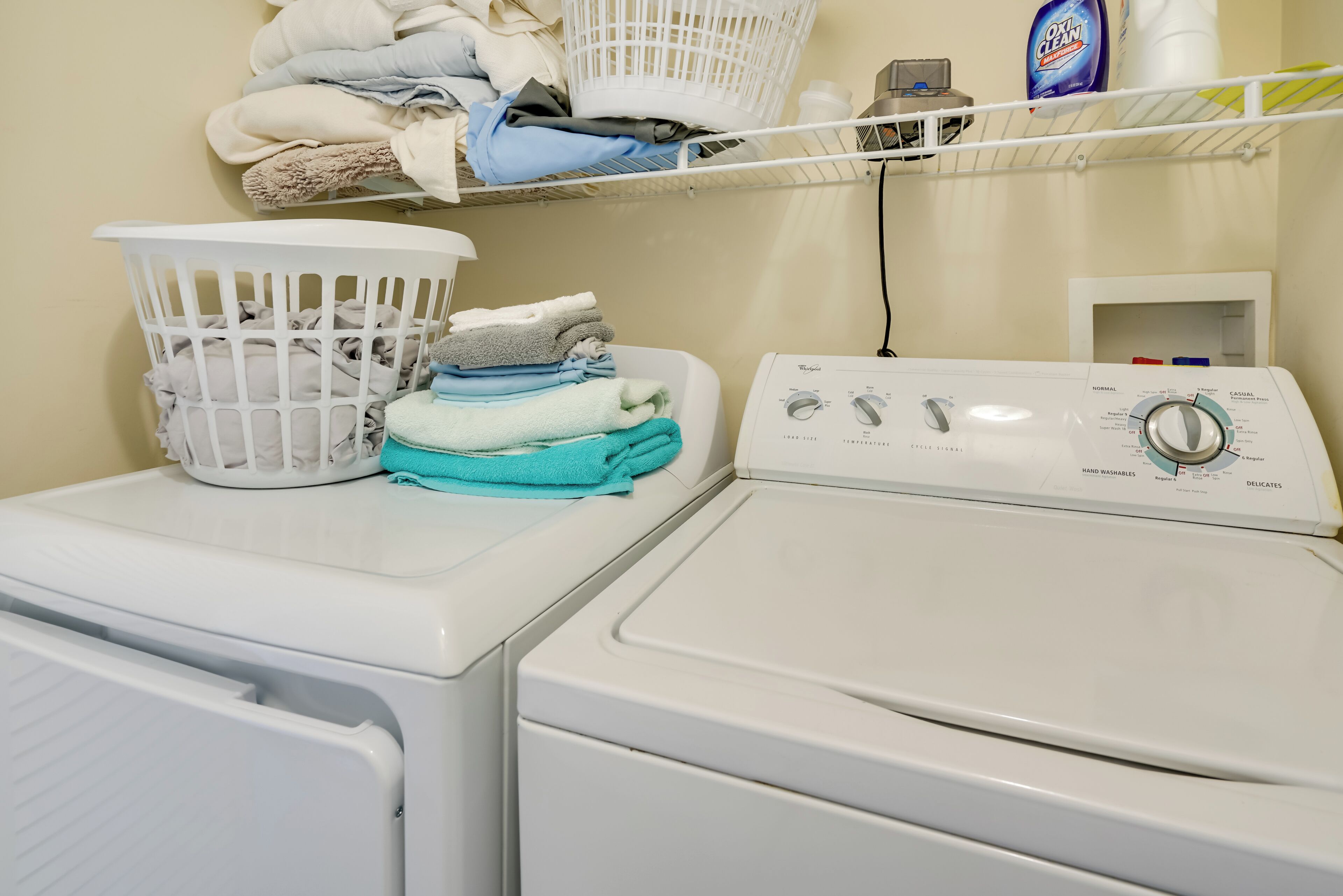 A front-loading washing machine with a control panel, a white laundry basket, and folded towels on top.