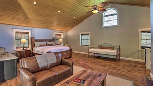 A spacious bedroom with a large bed, two smaller beds, a wooden ceiling, and a view of the outdoors through a window. - Game Room, Theater + Deck: Burnsville Cabin! (Burnsville)