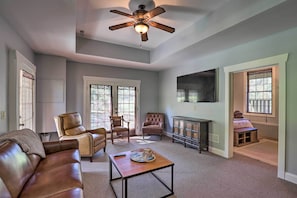 A spacious living room with a ceiling fan, leather sofas, a coffee table, and a TV mounted on the wall.