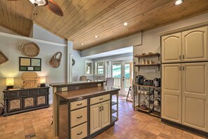 A kitchen with a wooden ceiling, a central island, and a dining area with chairs.