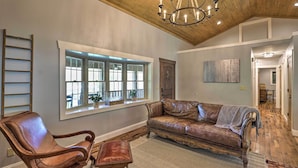 A spacious living room with a leather sofa, a wooden chair, and a chandelier. - Game Room, Theater + Deck: Burnsville Cabin! (Burnsville)