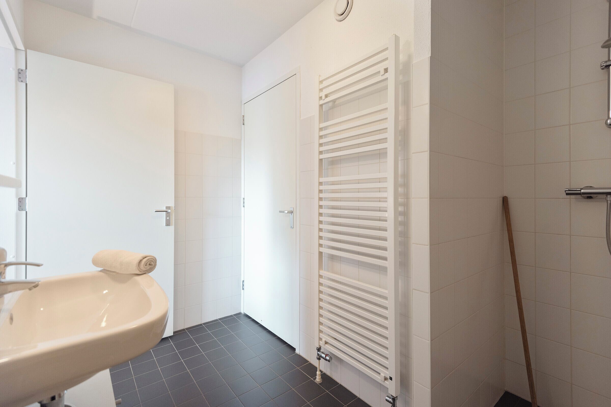 Een badkamer met een wastafel, een handdoek, een witte deur en een witte handdoekhouder.