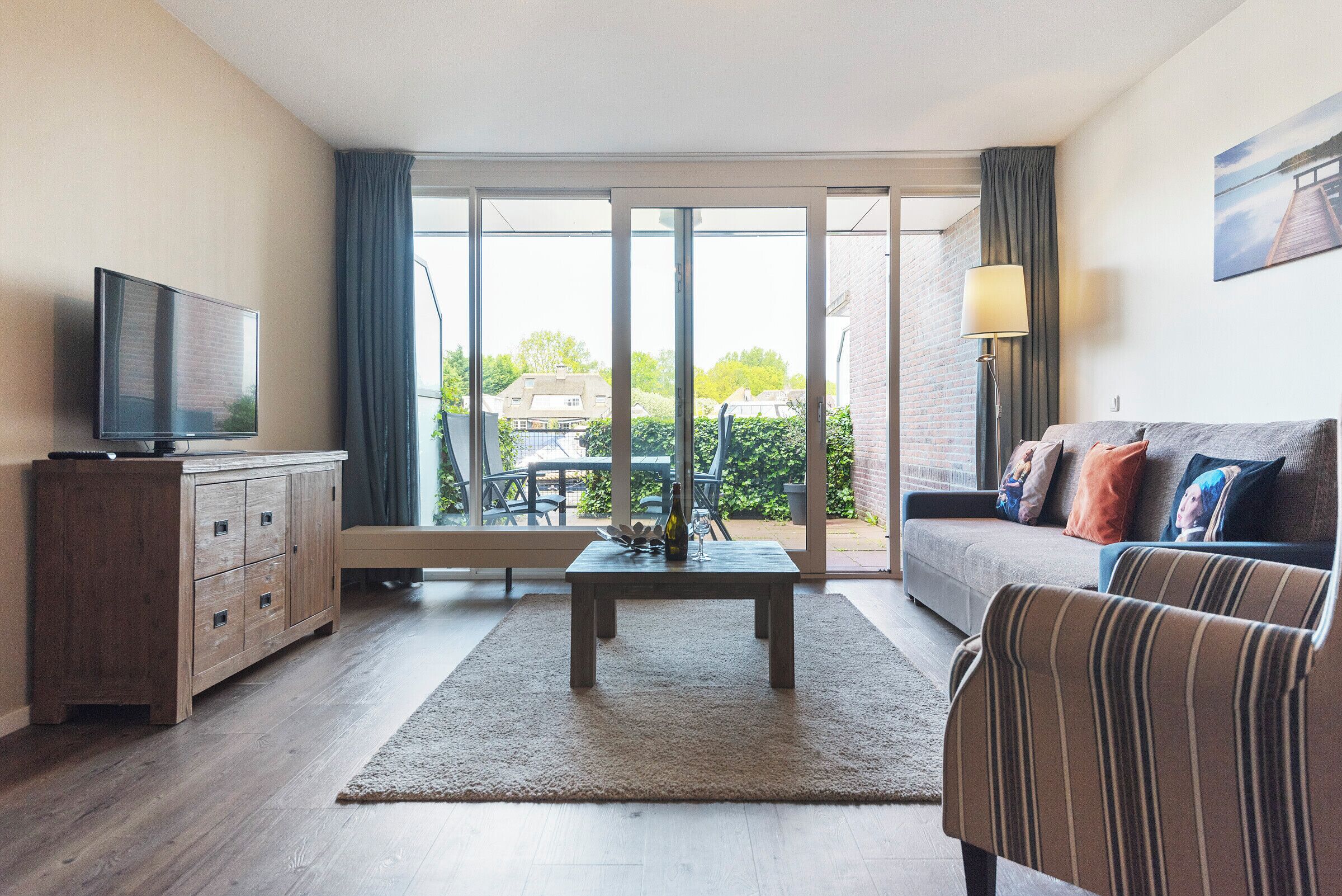 A living room with a television, a wooden cabinet, a sofa, a coffee table, and a view of the outdoors through a sliding glass door.