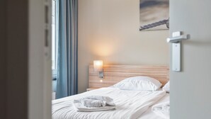 Una habitación de hotel con una cama bien hecha, una lámpara de noche y vistas al exterior.