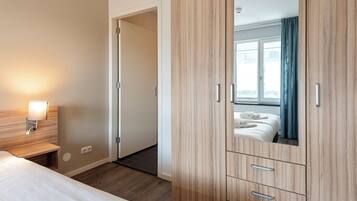 Een hotelkamer met een bed, een houten kledingkast, een nachtkastje met een lamp en uitzicht door een raam met gordijnen.