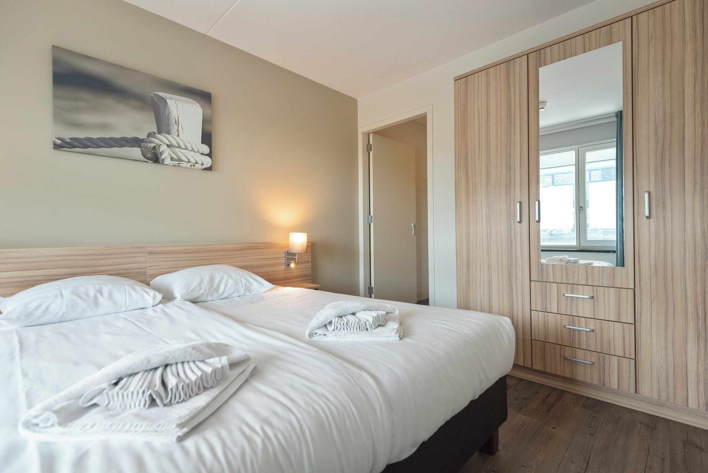 Une chambre d’hôtel avec un grand lit, une armoire en bois, un tableau au mur et une table de chevet avec une lampe.