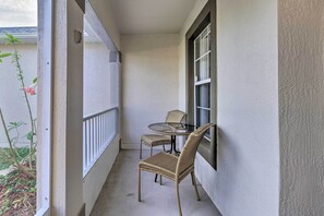 Een klein balkon met een glazen tafeltje en twee rieten stoelen.