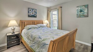Une chambre à coucher avec un lit en bois, deux tables de chevet avec des lampes, un ventilateur de plafond et deux tableaux aux motifs floraux accrochés aux murs.