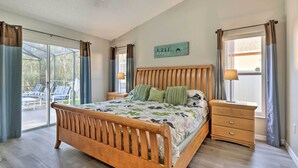 Une chambre à coucher avec un lit en bois, une table de chevet, une fenêtre avec des rideaux et une vue sur un espace extérieur aménagé pour s’asseoir.