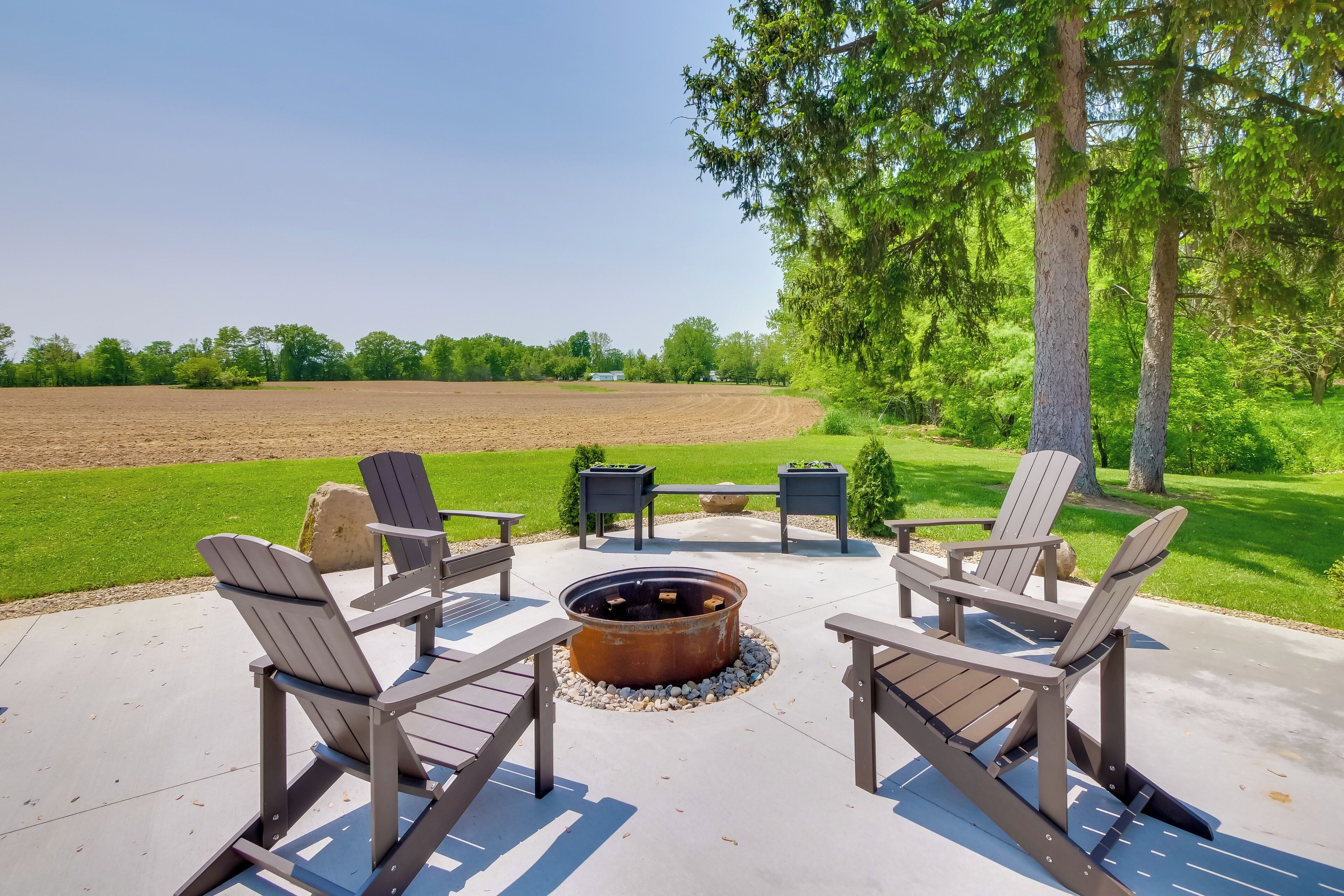 Eine Terrasse im Freien mit Adirondack-Stühlen, einer Feuerstelle und Blick auf ein Feld.
