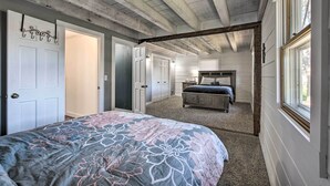 Une chambre à coucher avec un grand lit, un plafond en bois et une vue sur une autre pièce par une porte ouverte.