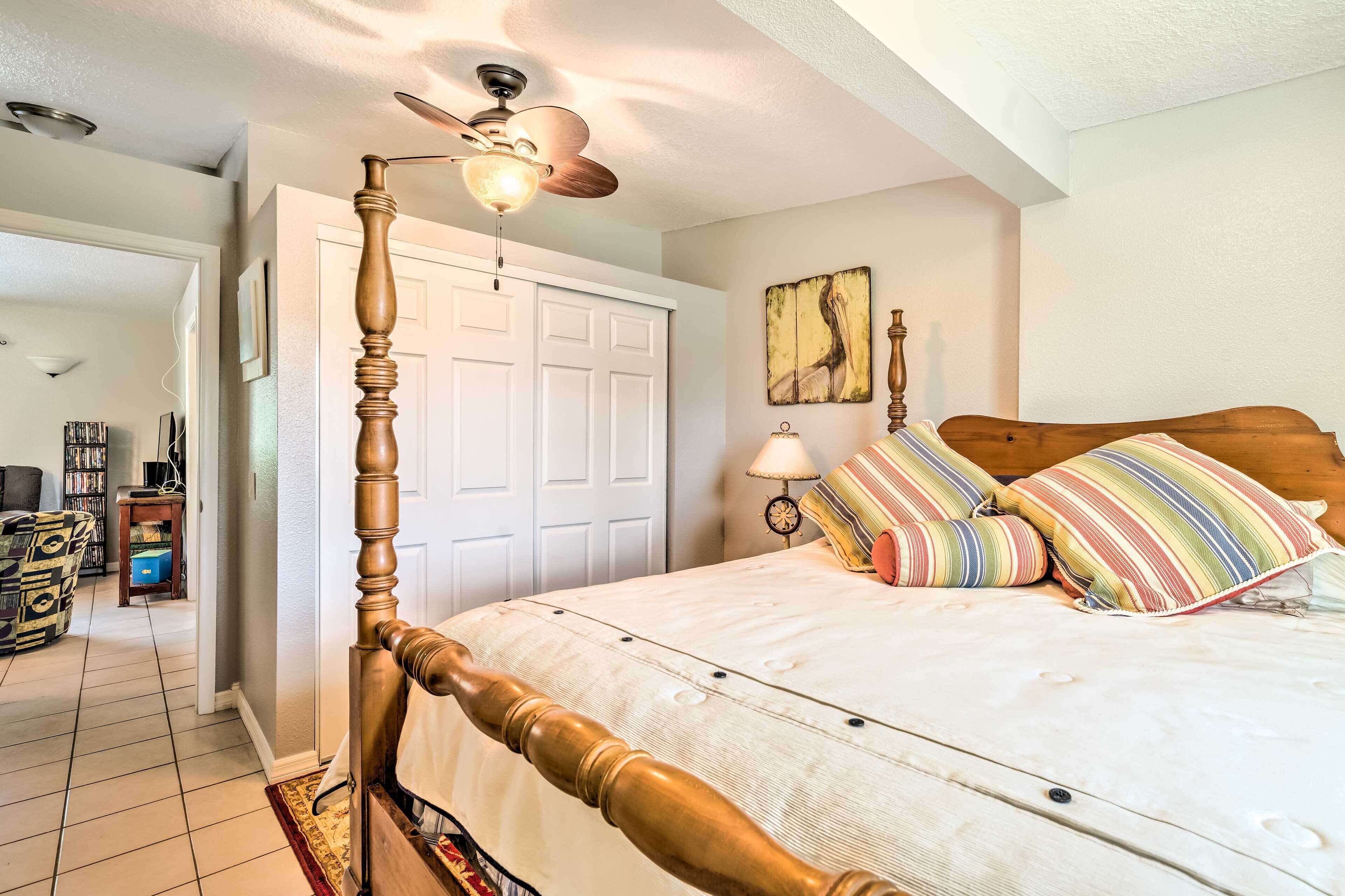A bedroom with a wooden bed frame, a ceiling fan, a white door, and a bedside table with a lamp.