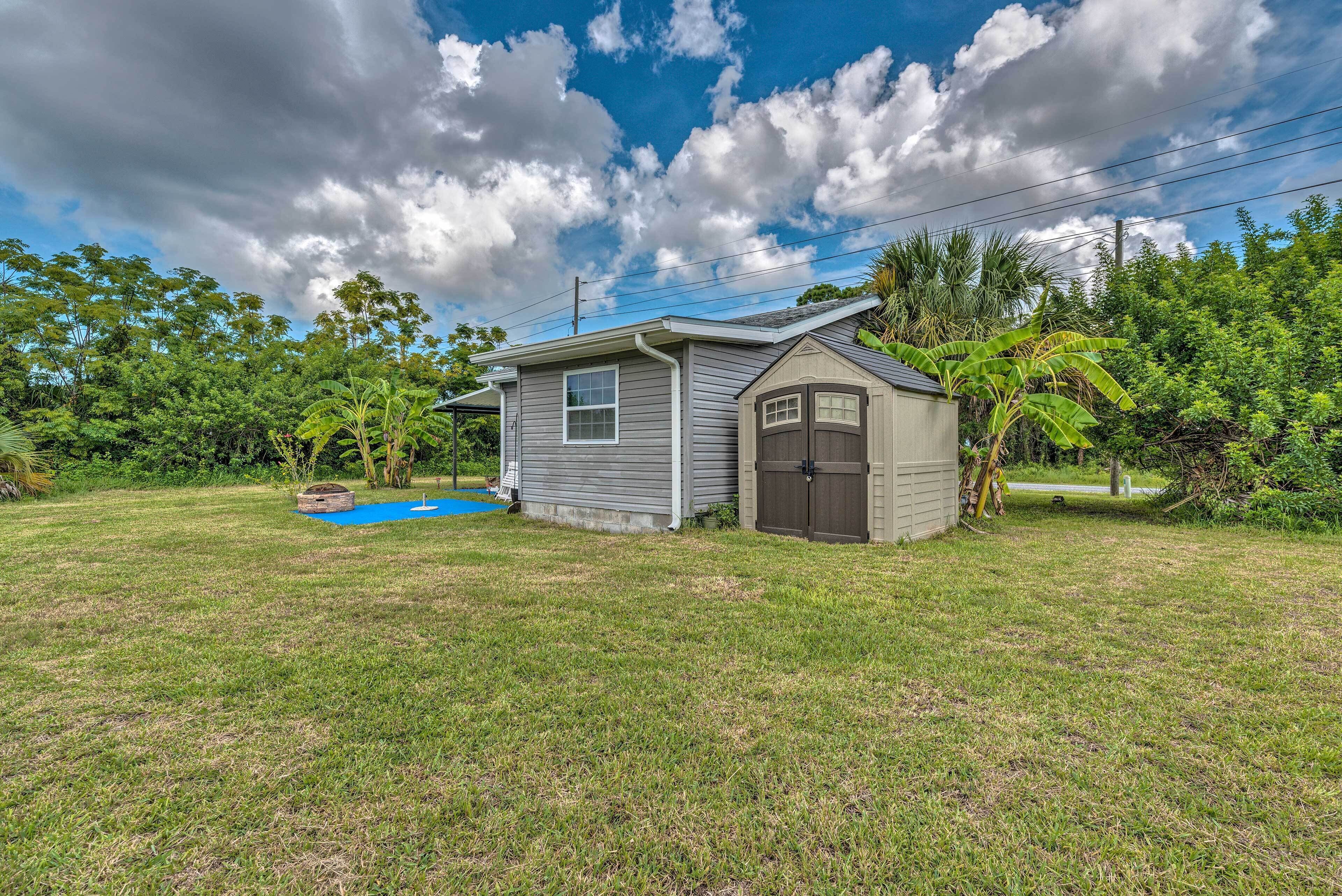 A small, single-story house with a shed, surrounded by a grassy yard and dense foliage.