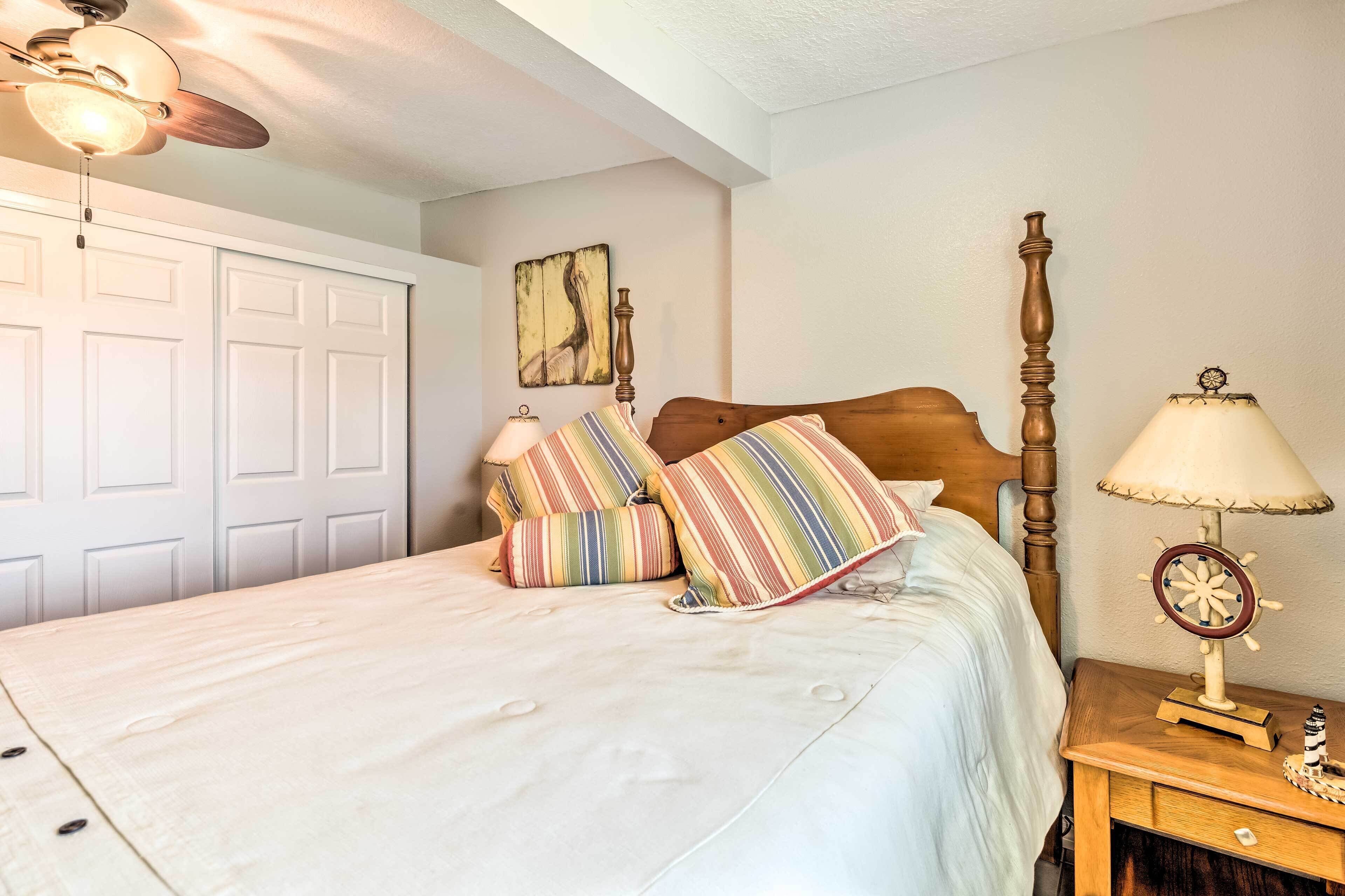 A neatly made bed with striped pillows, a wooden headboard, a nightstand with a lamp, and a ceiling fan.