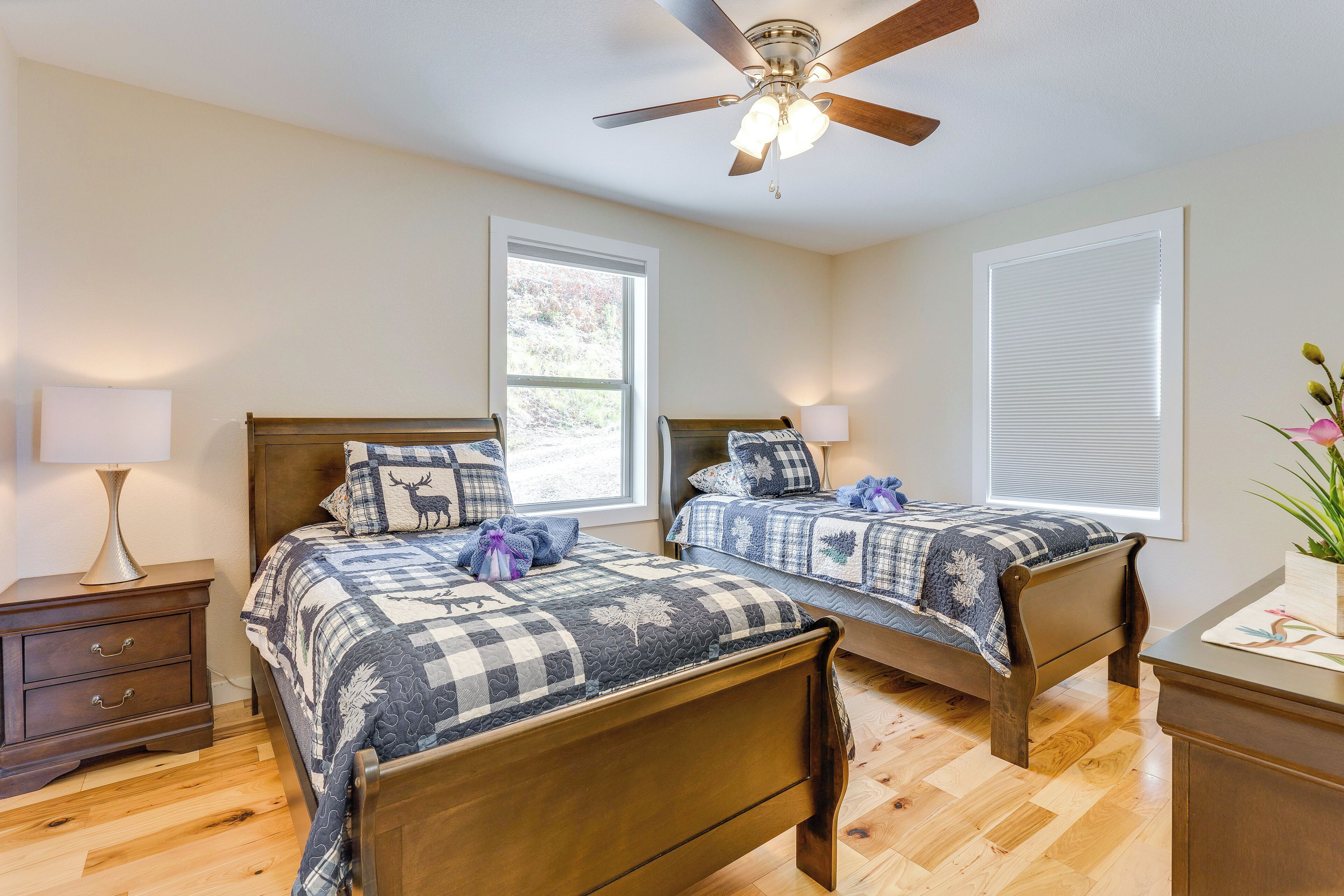 A bedroom with two beds, a ceiling fan, a nightstand, and a window with blinds.