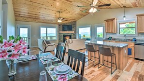 A spacious living area with a wooden ceiling, a fireplace, a stone accent wall, and large windows offering a view of the outdoors. - 'mountain Sky Escape' Murphy Cabin w/ Mtn Views (Murphy)