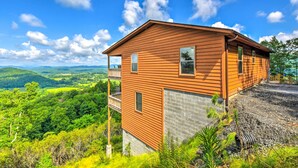 A wooden cabin with a balcony, surrounded by lush greenery and a clear blue sky. - 'mountain Sky Escape' Murphy Cabin w/ Mtn Views (Murphy)