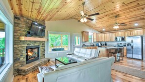 A modern living room with a stone fireplace, a flat-screen TV, and a white leather sofa. - 'mountain Sky Escape' Murphy Cabin w/ Mtn Views (Murphy)