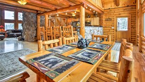 A wooden interior with a long dining table, chairs, and a stone wall.