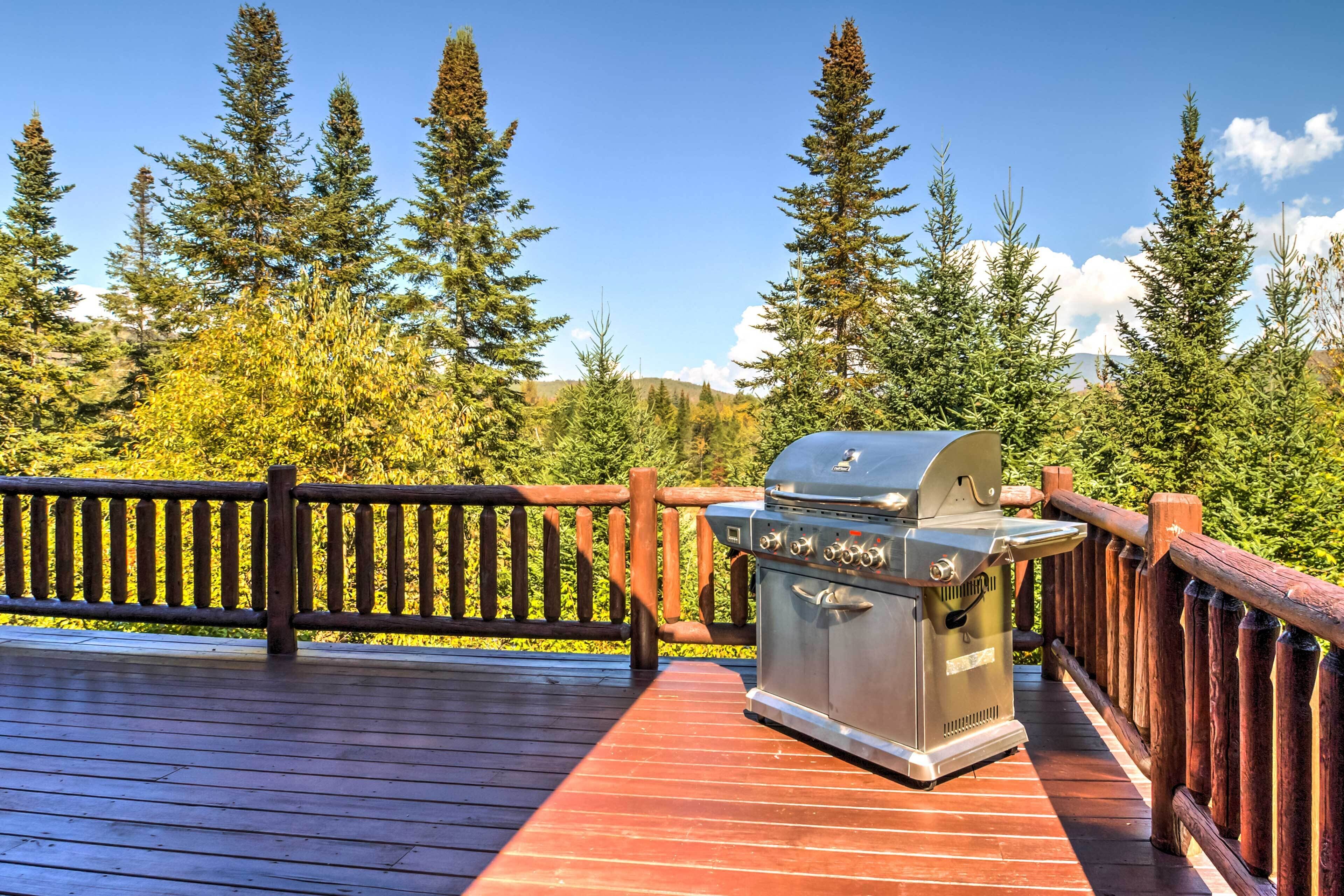 Un barbecue installé sur une terrasse en bois, avec une rambarde également en bois, le tout entouré d’arbres.