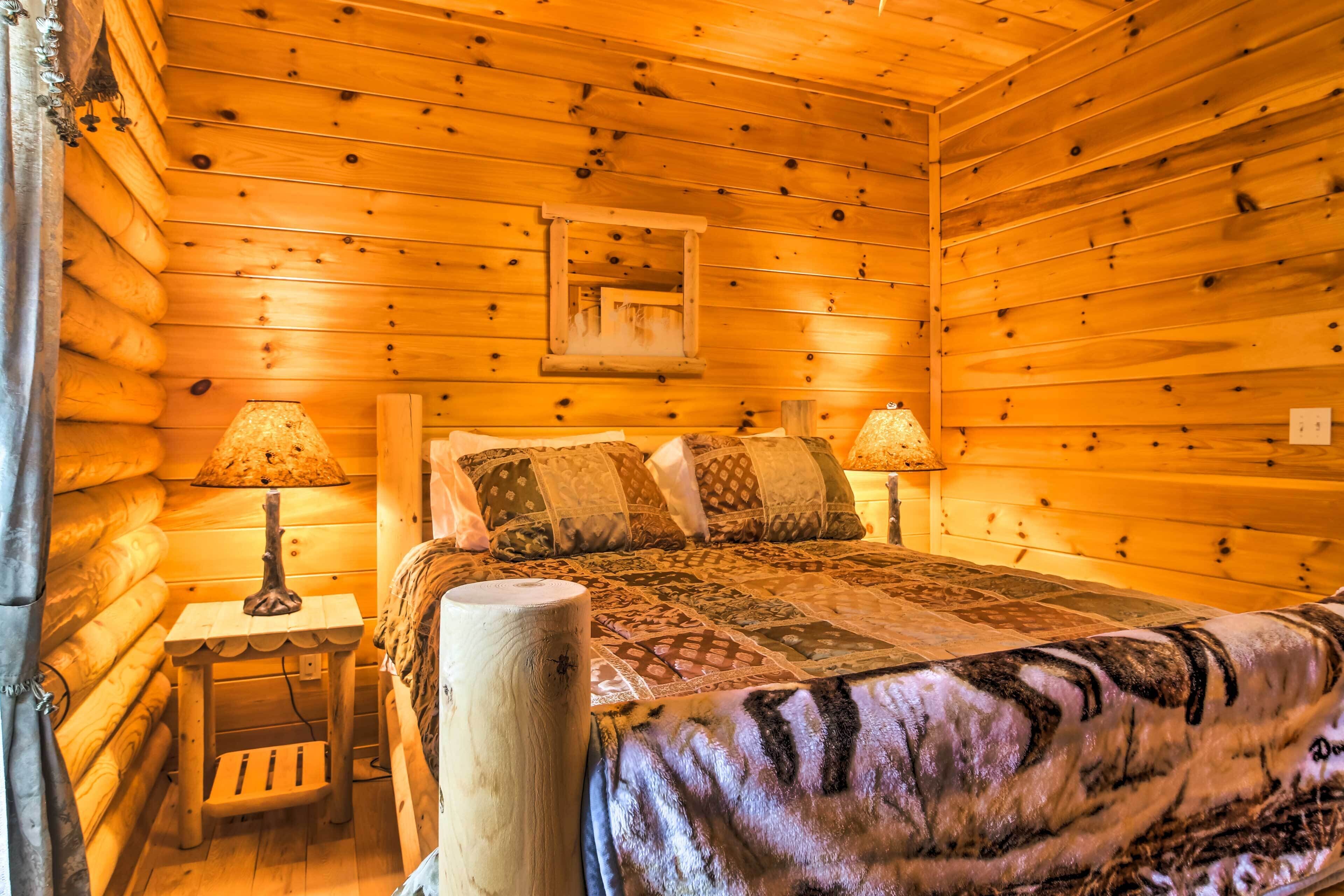 A log cabin bedroom with a wooden bed, two bedside lamps, a small wooden nightstand, and a mirror on the wall.