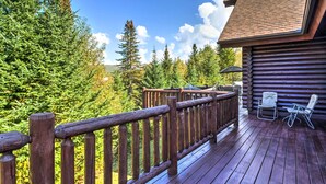 A wooden deck with a railing, overlooking a forested area and a cabin with a chimney.