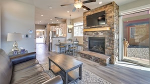 A spacious living room with a stone fireplace, a ceiling fan, and a large TV mounted above it.