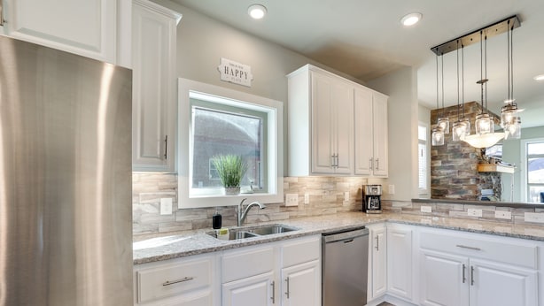 A modern kitchen with white cabinets, stainless steel appliances, and a stone backsplash.