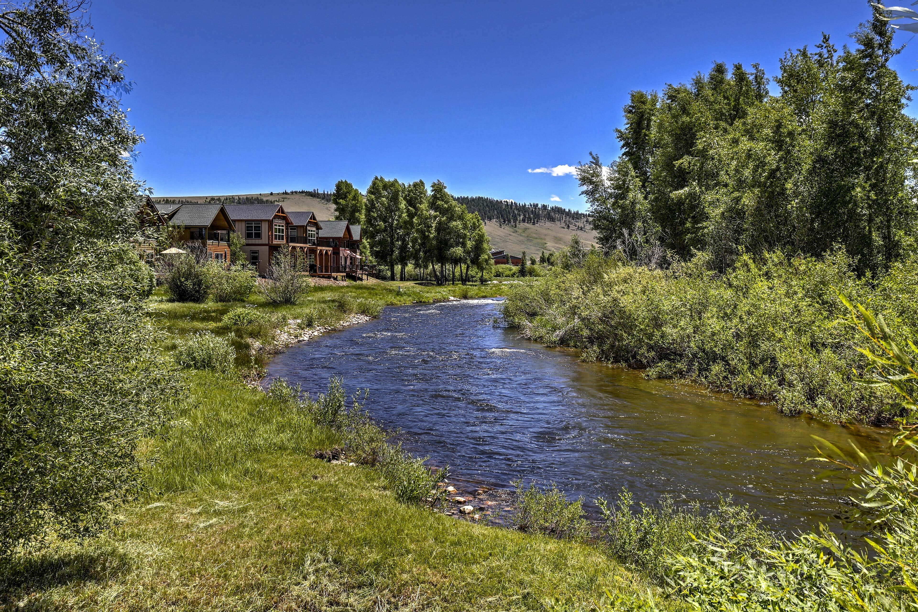 A lodge with a river running through its grounds, surrounded by dense forest and hills.