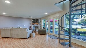 A spacious living room with a fireplace, a sofa, a dining area with outdoor view, and a staircase. - Lakefront Montgomery Home w/ Porch & Dock! (Montgomery)