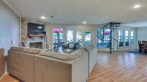 A spacious living room with a beige sectional sofa, a flat-screen TV mounted on a stone wall, and a wooden floor. - Lakefront Montgomery Home w/ Porch & Dock! (Montgomery)