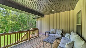 A covered deck with a wooden railing, a sofa with cushions, and a small table. - New Everything! Comfy Home w/ Deck & Trail Access! (Bella Vista)